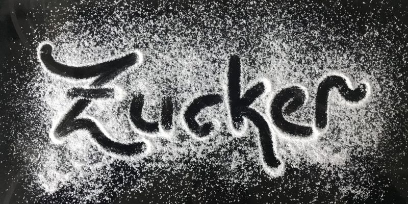 Das Wort Zucker mit Zucker auf einer schwarzen Unterlage geschrieben